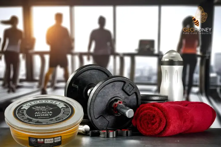 A jar of acacia honey with a wooden spoon on top, surrounded by fitness equipment such as dumbbells and running shoes.